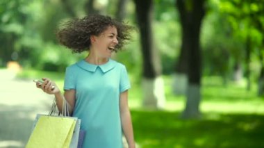 Kıvırcık kadın parkta alışveriş torbalarıyla yürüyor.