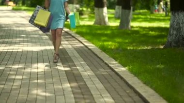 Kıvırcık kadın parkta alışveriş torbalarıyla yürüyor.
