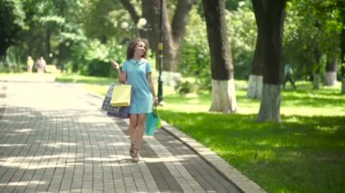 Kıvırcık kadın parkta alışveriş torbalarıyla yürüyor.