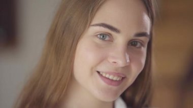 Sabah kameraya bakan farklı renkli gözleri ile sevimli genç gülümseyen kadın yakın çekim portre. Mutlu beyaz kadın yeni günü selamlıyor. Boş zaman, evde izin. Gerçek insanlar serisi.