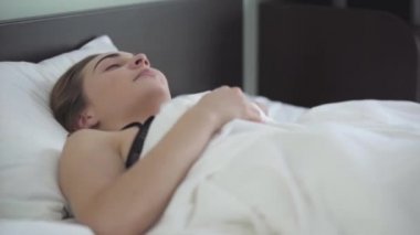 Genç güzel kadın sabah yatakta yatıyor. Kız uyandı ve kameraya gülümseyerek baktı. Evde boş zaman. Farklı renkli gözlü bir kız. Mutlu beyaz kadın yeni günü selamlıyor.