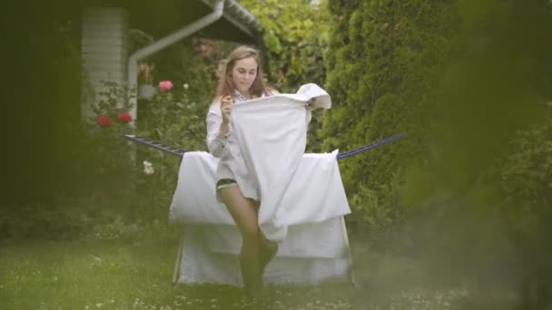 Cheerful cute young woman have fun singing and dancing at the backyard while doing house work with the linen. Washday, washing day. — Stock Video