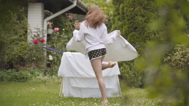 Attractive young woman dancing and rising legs at the yard while doing housework with the towel in hands. Active housewife having fine at home. Washday, washing day — Stock Video