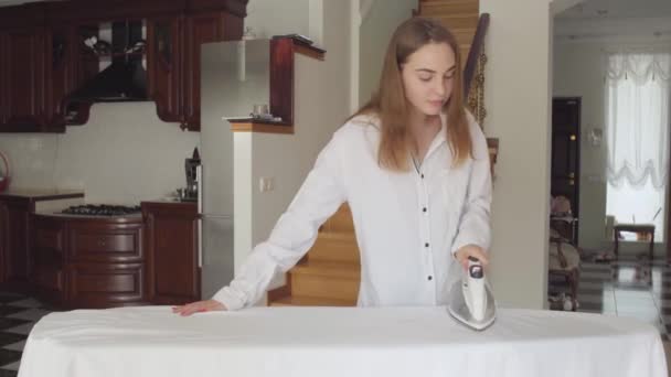 Mooie Kaukasische jonge vrouw dansen terwijl het huishoudelijk werk thuis. Leuke schattige huisvrouw strijken haar kleren op strijkplank. Wassen dag, wassen dag. Netheid en gezondheid, zorg. — Stockvideo