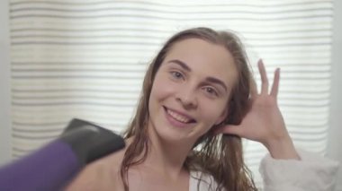 Çekici genç beyaz beyaz kadın portre kamera bakarak ve saç kurutma makinesi ile saçlarını kurutma sırasında dans. Farklı renkli gözleri olan güzel bir kız. Saç bakımı, güzellik konsepti. Yavaş çekim.