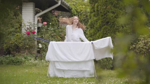 Ganska glad ung kvinna har roligt att sjunga och dansa på bakgården medan du gör husarbete med linne. Tvättdag, tvätt dag. — Stockvideo