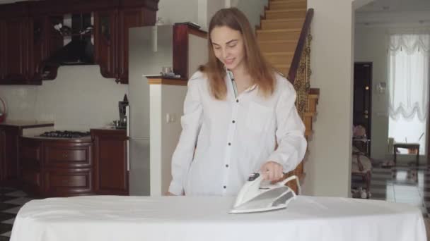 Aantrekkelijke jonge vrouw dansen terwijl ze thuis huishoudelijk werk doen. Actieve positieve huisvrouw strijken haar kleren op strijkplank. Wassen dag, wassen dag. Netheid en gezondheid, zorg. — Stockvideo