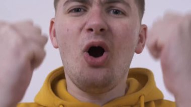 Futbol takımı için körükleyen, yumruklarını sıkan, duygularını ifade eden genç bir adamın yakın çekim. Eğlence kavramı, ifade, kendini ifade etme. Sorun cilt ve akne.