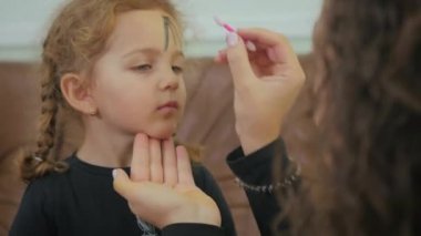 Kıvırcık kızı Cadılar Bayramı partisine hazırlayan kadının videosu. Kadın yüzü makyaj yapar.