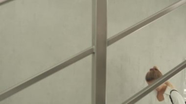 Beyaz bluzlu güzel sarışın ve merdivenlerde küçük siyah sırt çantalı. Çekici genç bir kadın elinde suyla bir şişe tutuyor. Güzel genç bir kadın ayna duvarının yanından geçiyor ve aynalara yansıyor..