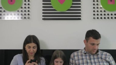 Kamera bir aşağı bir yukarı hareket ediyor. Genç bir aile, büyük yeşil bir yatakta yatıp aletlerini kullanıyor. Aileler aletlerini bir kenara bırakıp kızlarına sarılıyorlar. Kız gülümsüyor ve tableti kullanmaya devam ediyor..