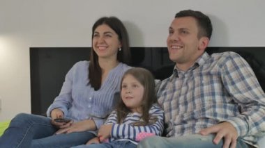 Genç, mutlu bir aile yatak odasında büyük bir yatakta yatıyor. Küçük kız ailesinin ortasında yatar. Genç bir kadın uzaktan kumandayla televizyondaki kanalları değiştiriyor. Mutlu, genç bir aile gülüyor..