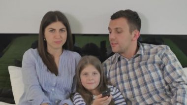 Genç, mutlu bir aile yatak odasında büyük bir yatakta uzanıyor ve kameraya bakıyor, tıpkı televizyondaki gibi. Küçük kız ailesinin ortasında yatar. TV 'nin kanallarını uzaktan kumandayla değiştiren tatlı bir kız. Anne kızından kanalı değiştirmesini istemiş..