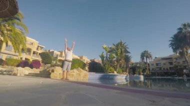 Genç sporcu, havuz kenarındaki tatil köyünde sabah egzersizi yapıyor. Kafasında havlu olan bir adam ellerini kaldırdı ve güneşe kapalı gözlerle baktı. Çekici bir adam ellerini ortaya koyar ve gözlerini açar..