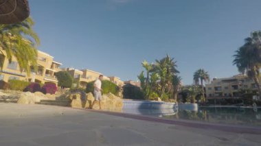 Genç adam yüzme havuzuna gelir, ileri geri adımlar atar. Gömlekli genç adam aniden suya sol bacağı kameraya çarpıp gülümsüyor. Su damlaları kameraya çarpıyor..