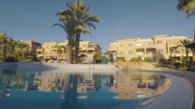 Adam havluyu omzuna koydu ve telefona cevap verdi. Genç adam telefonda konuşuyor ve yüzme havuzunun yanında yürüyor. Merdivenlerden inen ve havuzun kenarına gelen adam. Gülümseyen ve etrafa bakan adam.