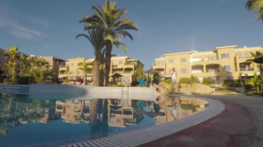 Genç adam telefonda konuşuyor ve yüzme havuzunun yanında yürüyor. Merdivenlerden inen ve havuzun kenarına gelen adam. Adam gülümsüyor ve kameraya yaklaşıyor. Adam havuzun kenarındaki kameranın yanından geçiyor..