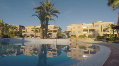 Genç adam güverte sandalyesini alıp yüzme havuzunun yanına koydu. Çekici adam havluyu iskemleye koydu ve yüzme havuzuna geldi. Merdivenlerden inen adam, üzerine oturur, bacaklarını suya daldırır, gözlerini kapatır ve eğlencenin tadını çıkarır..