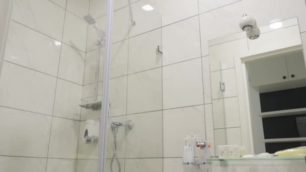 摄像机从上往下移动 浴缸和水池附近有一面大镜子 许多关于淋浴的细节都在白色的瓷砖上 有一次性剃须刀 洗发水小瓶 病人的淋浴帽 — 图库视频影像