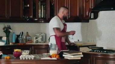 Genç adam evde mutfakta yemek pişiriyor. Kaslı aşçı bir şarap içer ve krepler hazır olduğunda bekler. Genç adam ev mutfağında krep pişiriyor. Kaslı adam krepli kahvaltı hazırlıyor..