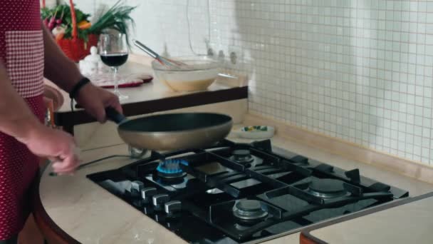 这个人开始在煎锅里做煎饼 那家伙把油放在热油锅里 用手拿着 铺在表面上 那个人打开炉子 年轻人在家里的厨房里做饭 — 图库视频影像