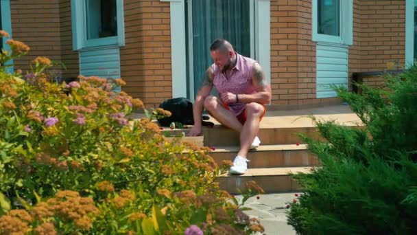 Νεαρός Κάθεται Στη Βεράντα Έξω Μαύρο Σκυλί Βρίσκεται Δίπλα Γενειοφόρο — Αρχείο Βίντεο