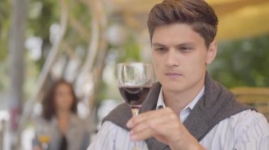 Yakışıklı genç adam sokak kafede kırmızı şarap içiyor. Dışarıda alkol ünkeyfini çıkaran adam. Müşteri masada oturup içecek tatıyor. Boş zaman, izin günü.