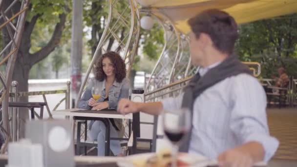 Im Vordergrund sitzt ein junger Mann, der Rotwein trinkt, und blickt auf eine attraktive Frau, die im Hintergrund im modernen Café flirtet. — Stockvideo