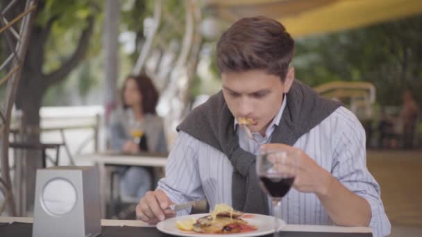 Pohledný muž pojídáním chutného masného jídla v pouliční kavárně a pití červeného vína. Dívka si vychutnával jídlo venku. Chlap, který střímá vidličkou a nožem. Volný čas venku — Stock video