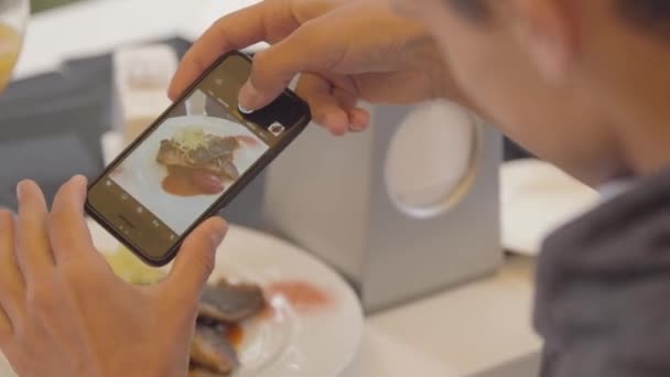 Närbild av ung man tar bild av sin fiskrätt med hjälp av mobiltelefon i restaurangen. Mannen njuter av sin mat avkopplande i kaféet. Fritid ensam — Stockvideo