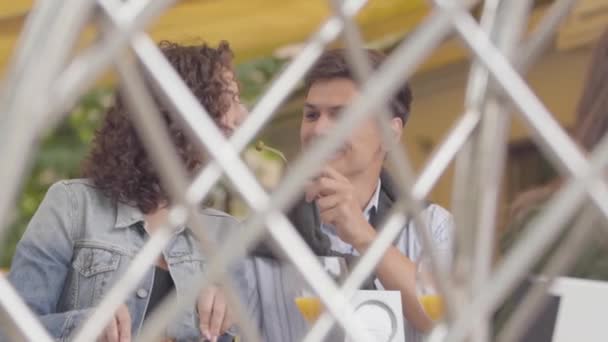 The happy couple enjoying their dinner relaxing in cafe. Handsome man sharing his food with girlfriend. Shooting from behind the fence. Leisure together, date concept. Slow motion. — Stock Video