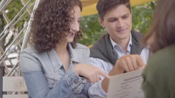 Compagnia di amici che leggono il menu in lingua russa scegliendo cibo in caffè o ristorante. Ragazzi che si incontrano al bar all'aperto. Tempo libero estivo. Rallentatore . — Video Stock