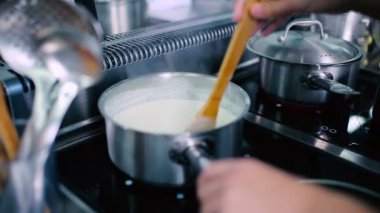 Aşçı ocakta tabak kaynatır. Aşçı ahşap kaşıkla yemeği karıştırır..