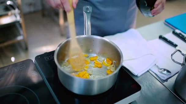厨师在炉边准备蔬菜 那人在锅里用热油把胡萝卜和洋葱煎了 然后把酒加到盘子里 厨师把蔬菜和木勺混合在一起 — 图库视频影像