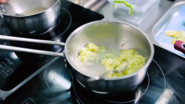 Yakın plan: Aşçı fırının yanındaki kasede püreyi karıştırıyor. Püre kaynıyor..