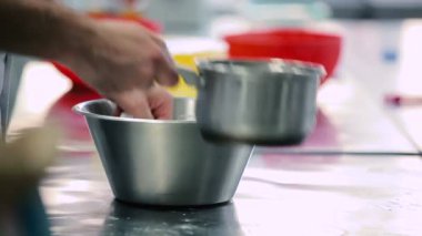 Adam mutfakta hamuru suyla un yoğuruyor. Adam una su ekliyor ve hamur plastik bıçakla karıştırılıyor..