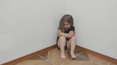 Odanın köşesinde oturan üzgün küçük kız. Küçük kız elleriyle kendine sarılıyor ve negatif kafa sallıyor. Tatlı küçük kızın gözünün yanında bir çürük var. Aile içi şiddetten sonra küçük bir kız. Çocuk ayağa kalkar ve gider..