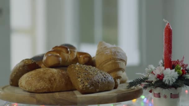 面包在桌上的装饰性蜡烛旁边旋转着 许多种类的面包和甜烘焙都在板上 装饰雪落在面包上 圣诞节期间 — 图库视频影像