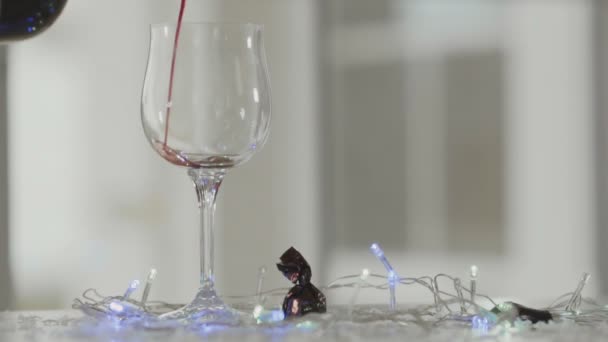 人間はゆっくりと赤ワインをワイングラスに注ぐ クリスマスライトを点滅させる休日の雰囲気を作成します — ストック動画
