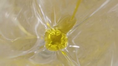 Bir bardağa zeytinyağı dök. İki zeytin yağın içine düşer. Yavaş çekimde. Yakın plan..