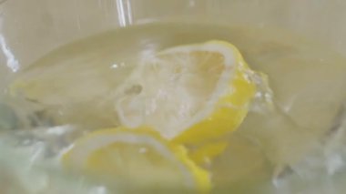 Limon parçası suyla dolu bir kaseye düşer. Kasenin etrafına bir sürü su damlası sıçrıyor. Yakın plan çekim. Yavaş çekim.