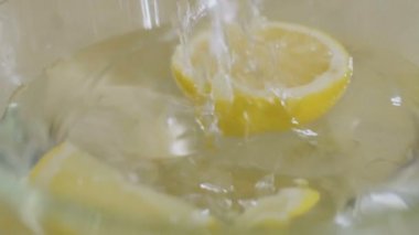 Limon parçası suyla dolu bir kaseye düşer. Kasenin etrafına bir sürü su damlası sıçrıyor. Yakın plan çekim. Yavaş çekim.