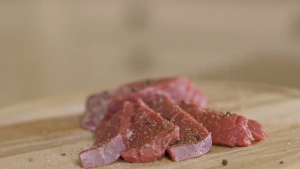 スパイスと塩は肉の生の部分に落ちます 台所で肉を調理する 接近中だスローモーション — ストック動画
