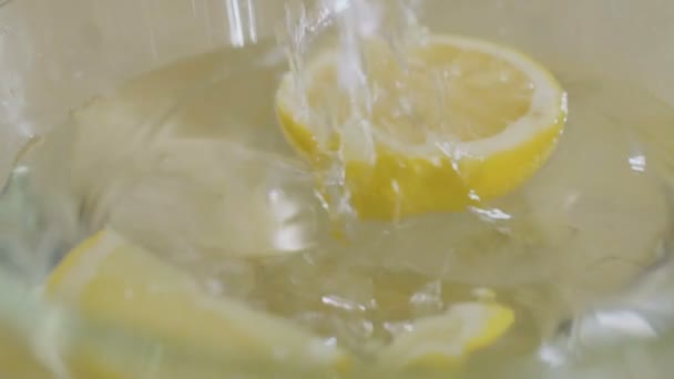 レモンの一片は水でボウルに落ちる たくさんの水がボウルの周りに飛び散っています 至近距離から撃たれたスローモーション — ストック動画