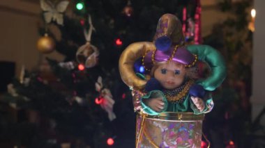 Güzel bir şaka oyuncağı. Güzel, parlak elbiseli oyuncak bebek sağa sola hareket ediyor. Arka planda Noel topları olan bir Noel ağacı. Yakın plan..