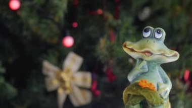 Oyuncak kurbağa figürü kameranın önünde dönüyor. Arka planda Noel topları olan bir Noel ağacı. Yakın plan..