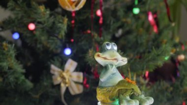 Küçük bir melek figürü kameranın önünde dönüyor. Avuç içleri katlanmış beyaz bir melek figürü. Arka planda Noel topları olan bir Noel ağacı. Yakın plan..
