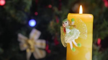 Yanan sarı Noel mumu kameranın önünde dönüyor. Arka planda Noel topları olan bir Noel ağacı. Yakın plan..