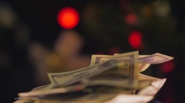 100 dolarlık banknotlar kameranın önünde dönüyor. Arka planda Noel topları olan bir Noel ağacı. Yakın plan..