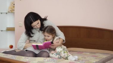 Anne ve tapılası kızı evde yatakta oturmuş kitap okuyorlar. Aile boş zamanlarını evde birlikte geçirir..